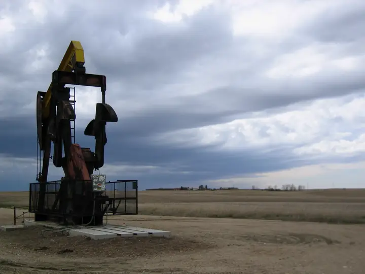 A pumpjack on a flat prairie well site under a dark, stormy sky.