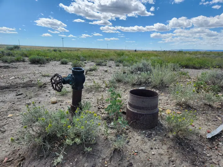 An open, unplugged orphan well with a rusted valve and a bare casing stub in sagebrush prairie in Toole County, Montana.